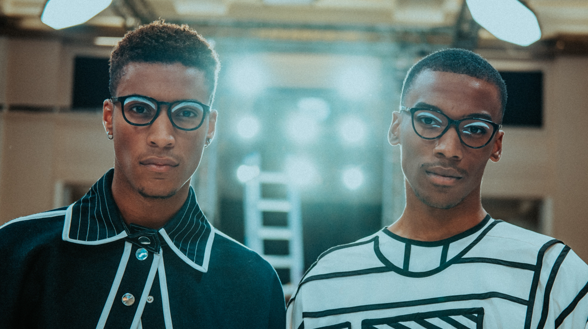 Two models wearing glasses and asymetrical shirts in front of a ladder